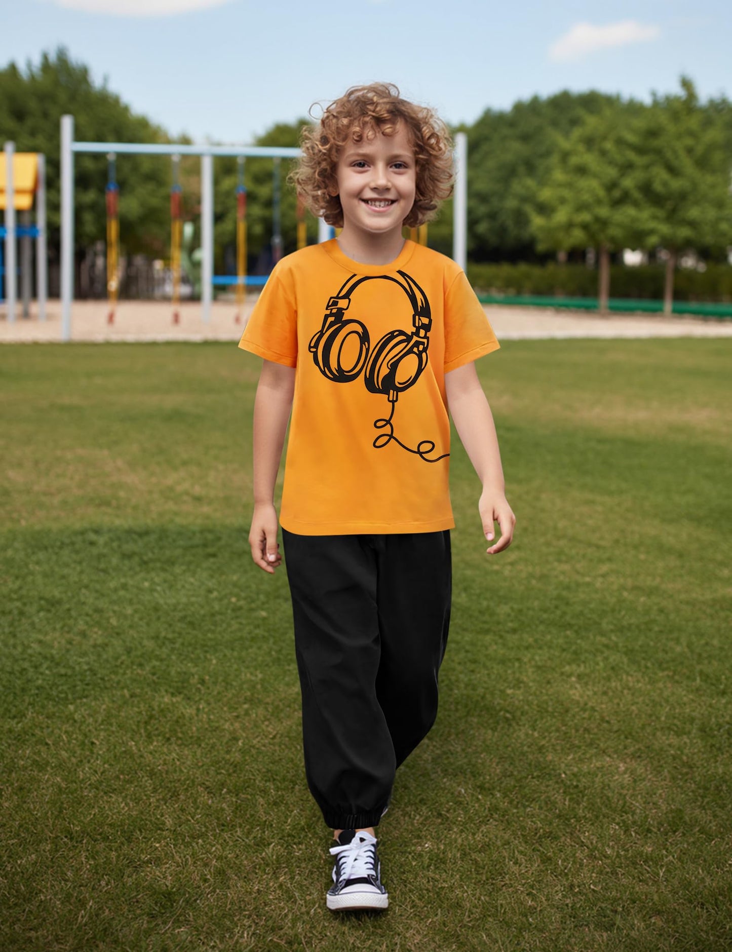 Child wearing an orange t-shirt with a black graphic design outdoors on grass