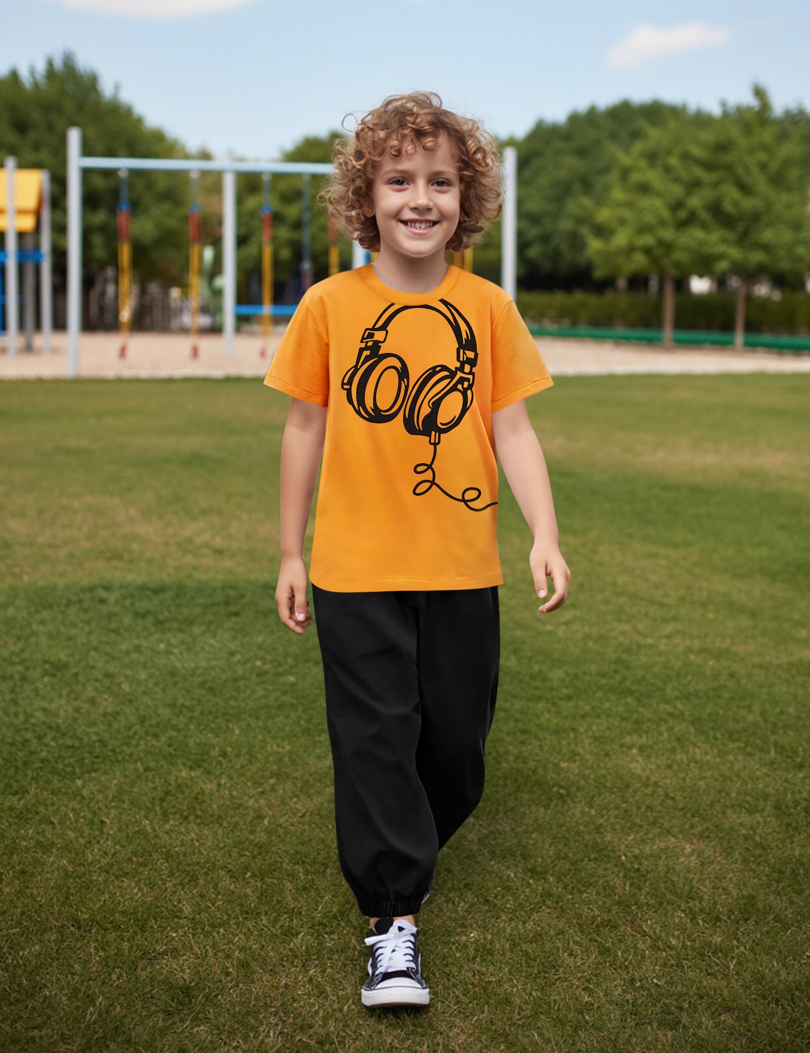 Child wearing an orange t-shirt with a black graphic design outdoors on grass