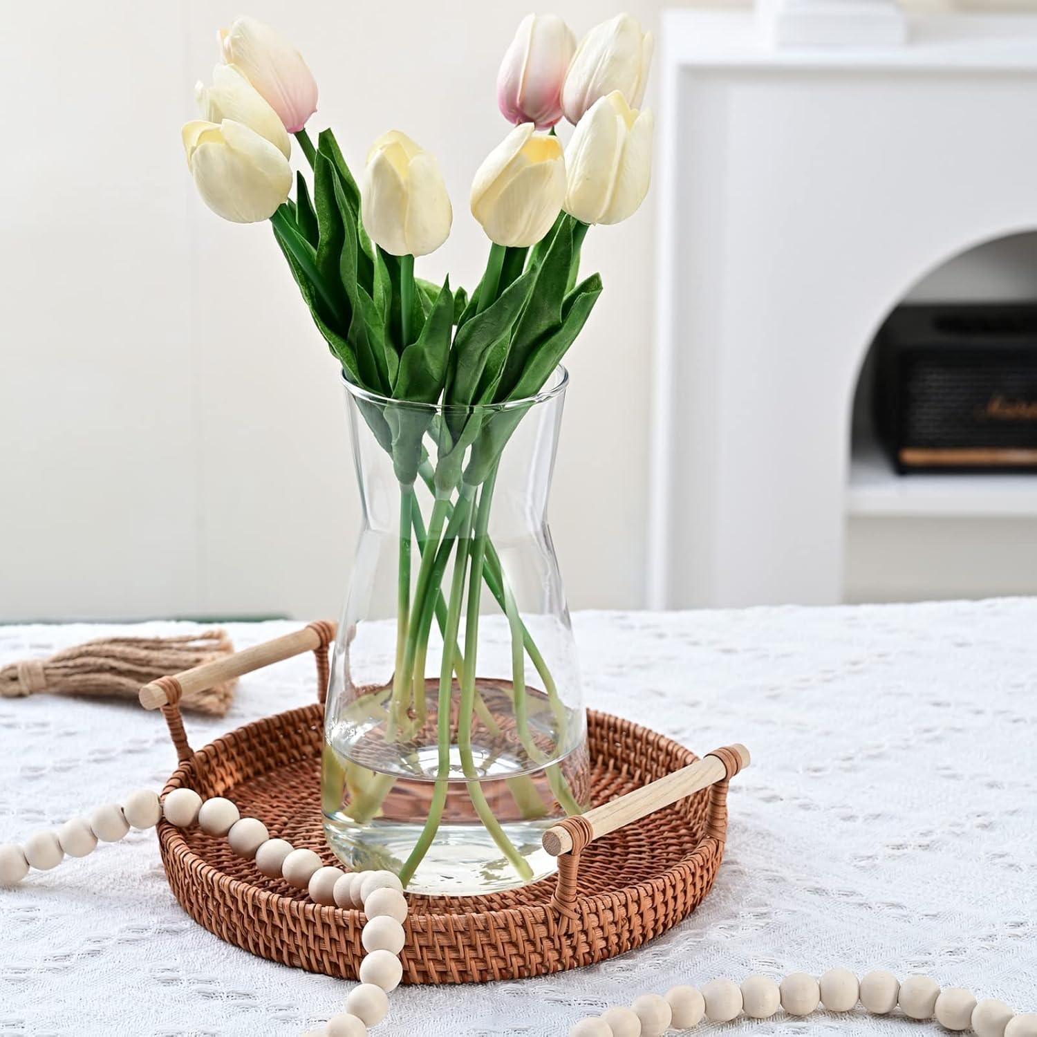 Clear vase with white tulips on a woven tray on a white surface