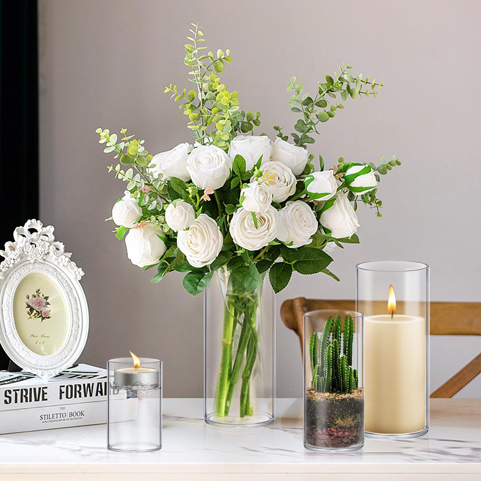 Bouquet of white roses and greenery in a vase with candles and a framed picture on a table.