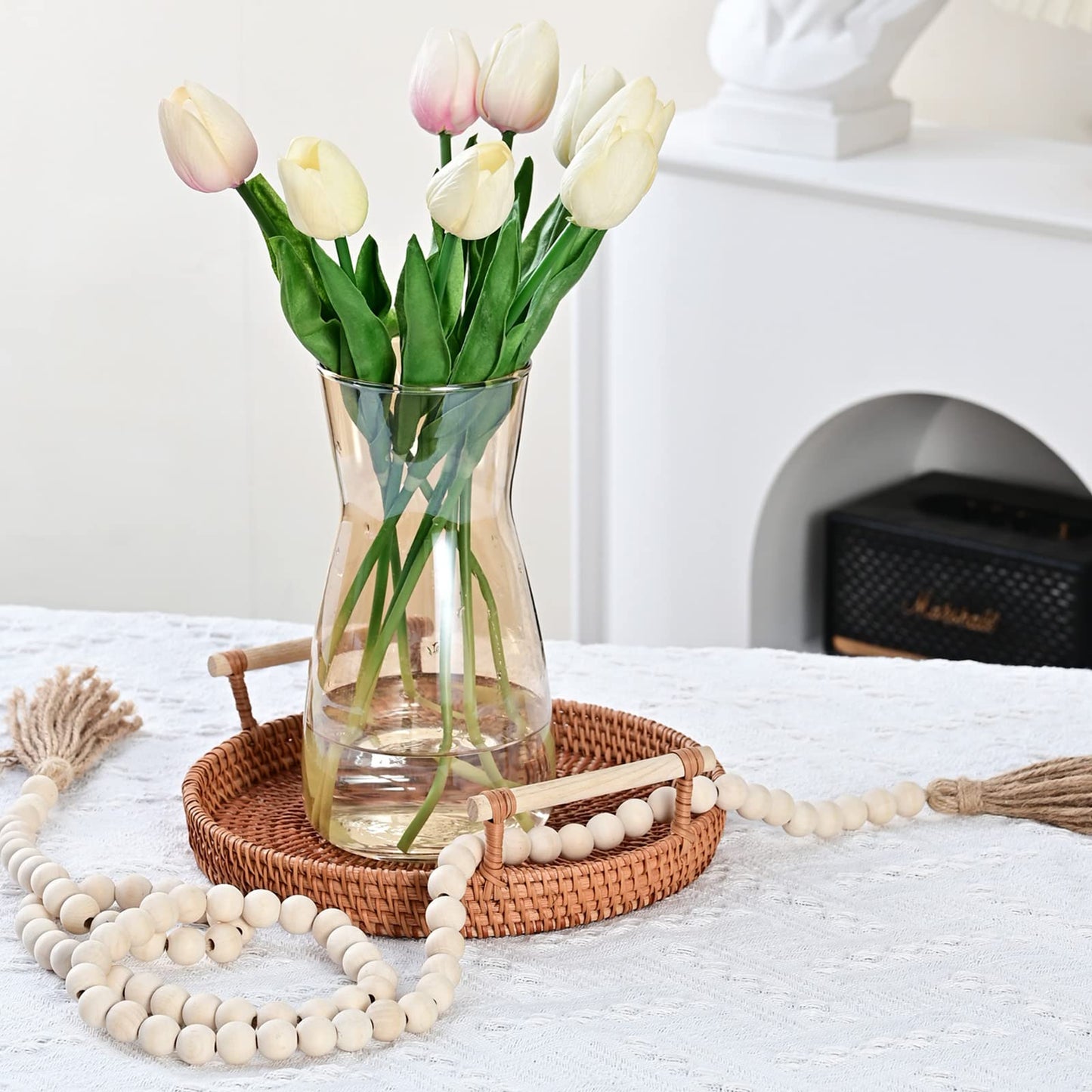 Clear vase with white and pink tulips on a wooden tray with beads, against a light background.