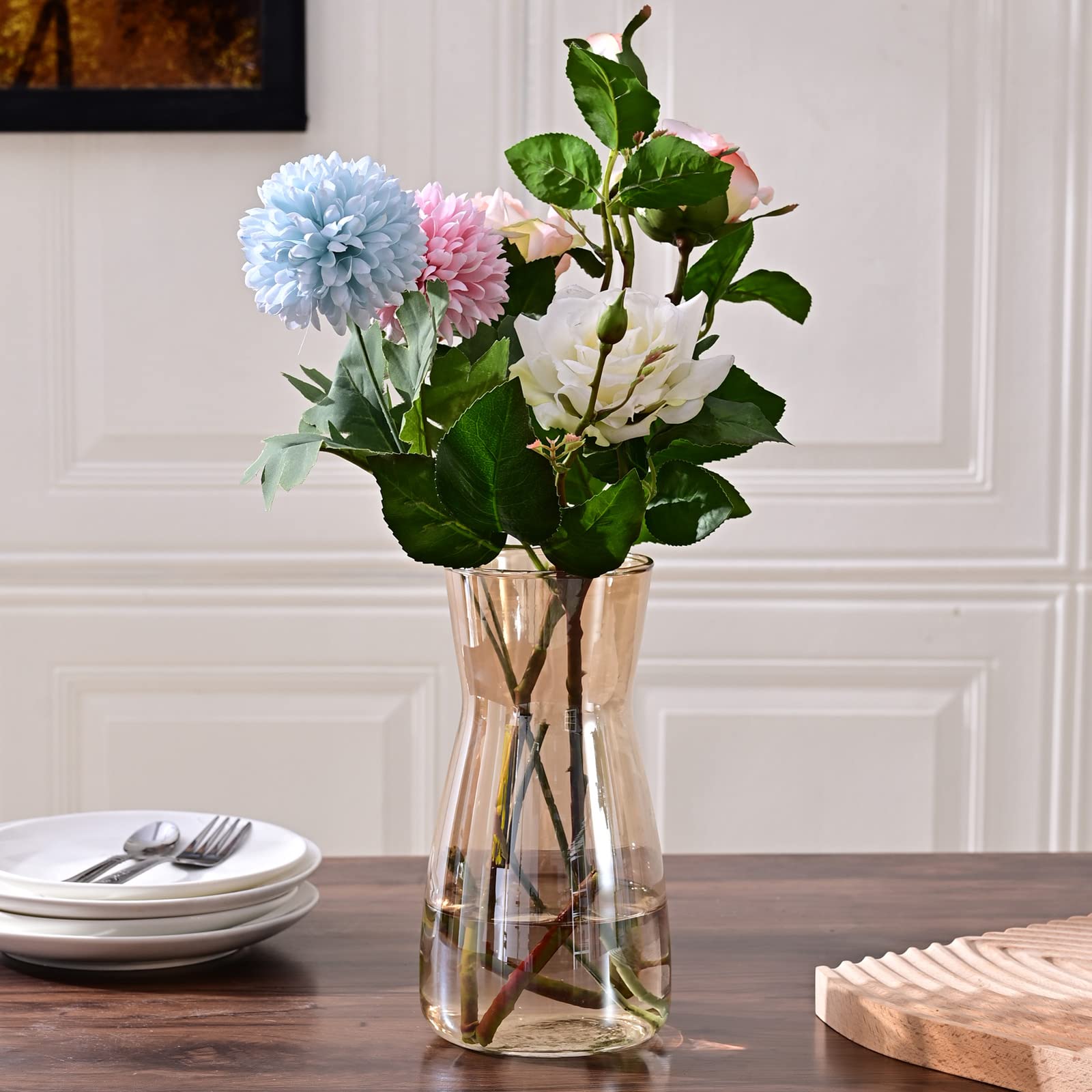 Clear vase with flowers on a wooden table against a white paneled wall.