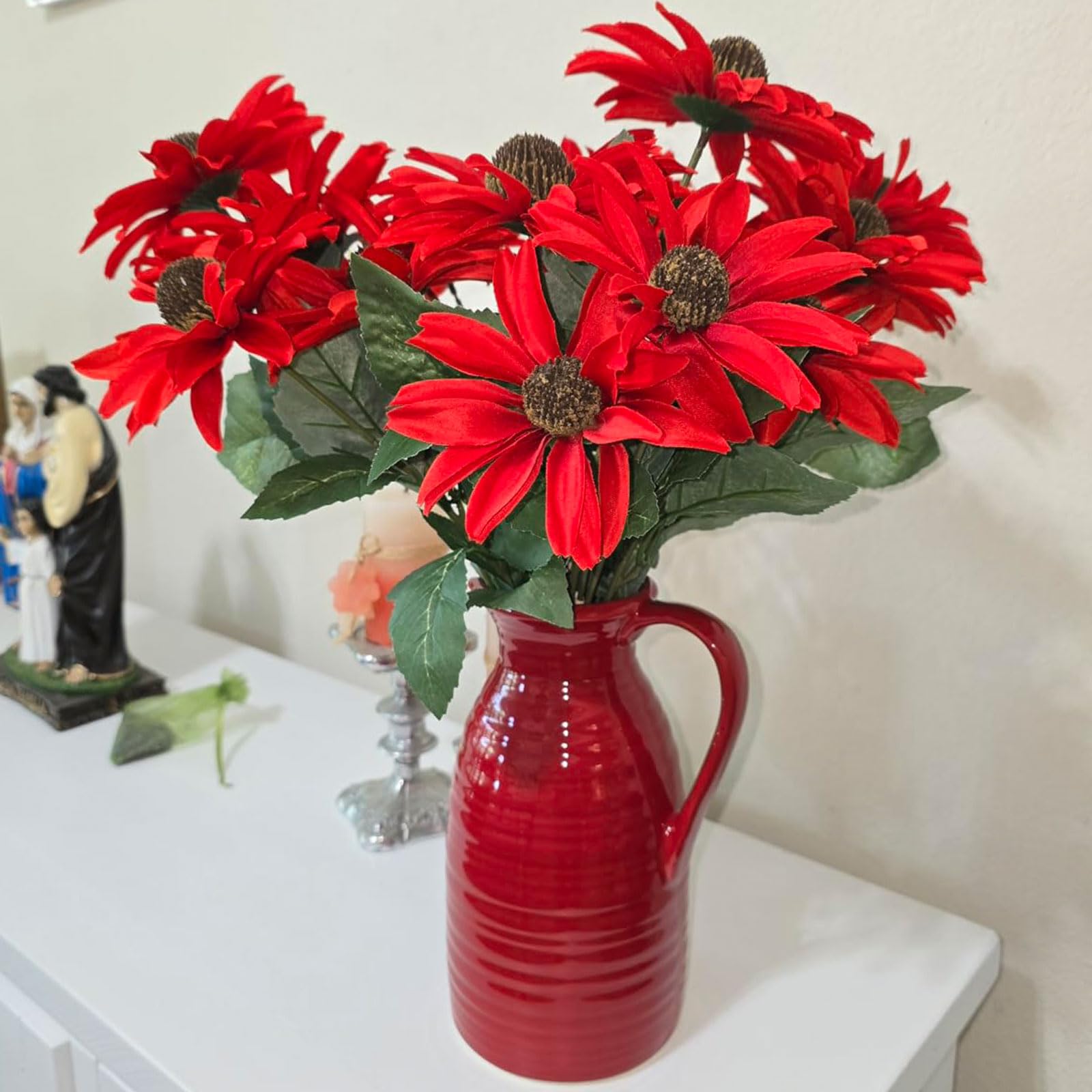 Red flowers in a red vase on a white surface with a neutral background