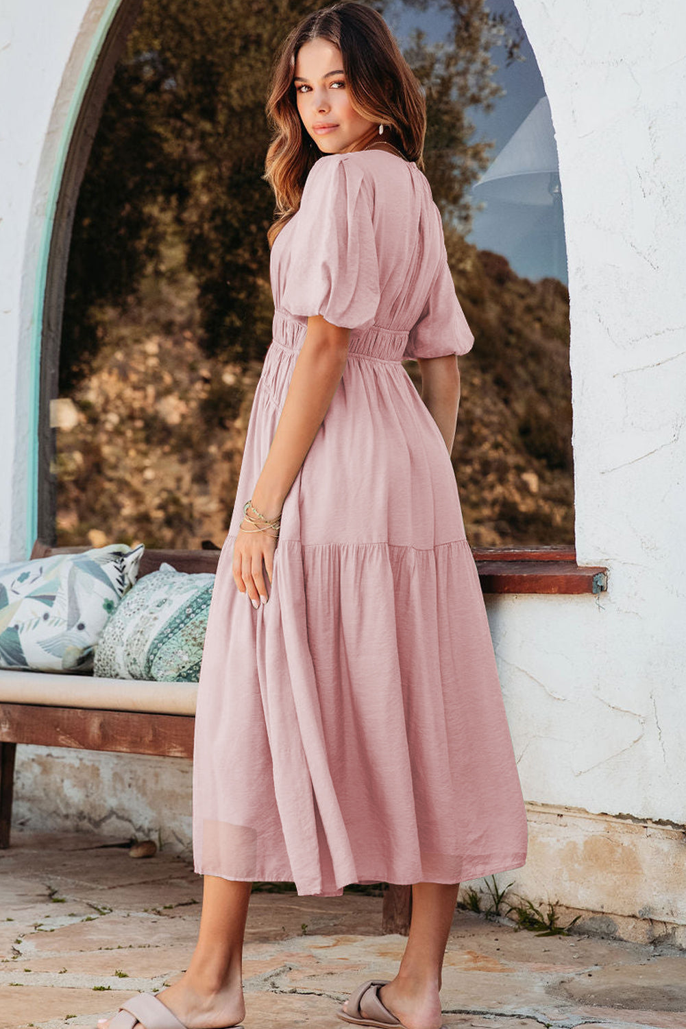 Woman in a pink dress standing in front of a white archway with greenery.