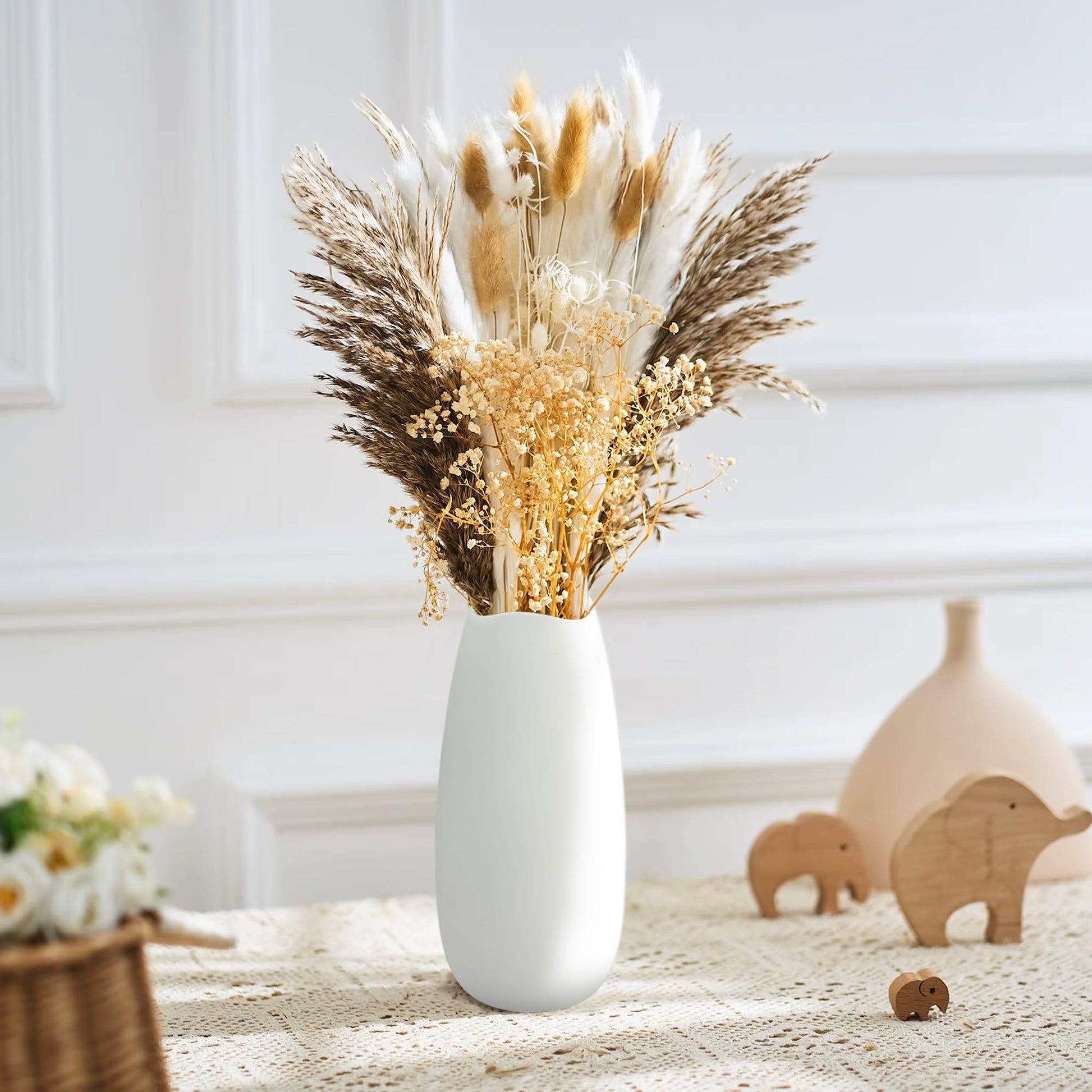 White vase with dried flowers on a textured surface with decorative elements.