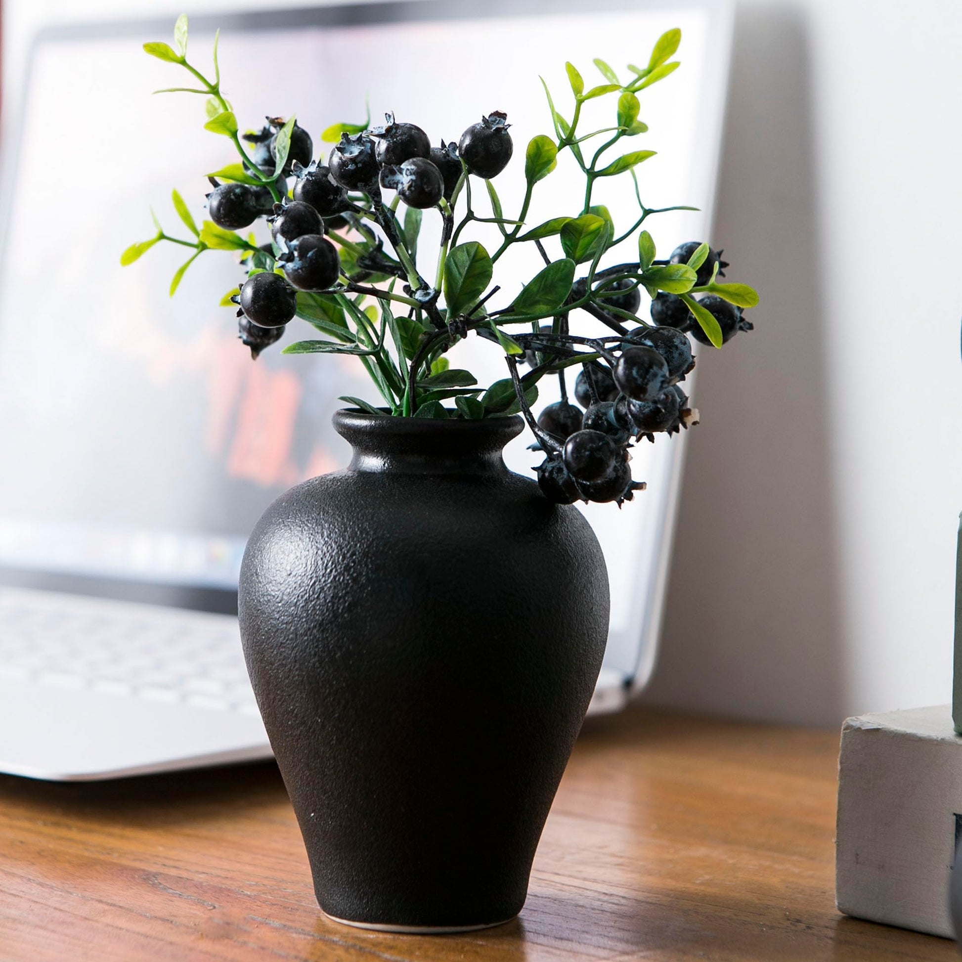 Black vase with greenery on a wooden surface