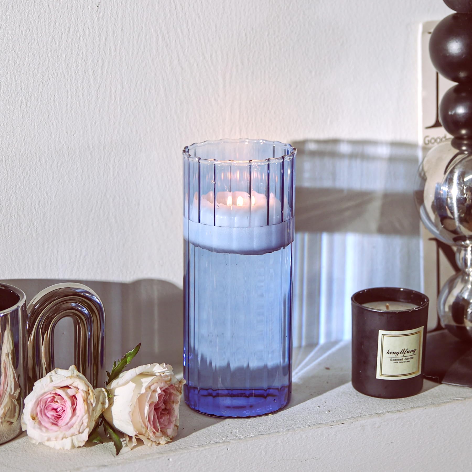 Blue candle holder with a lit candle on a surface with flowers and a decorative item.