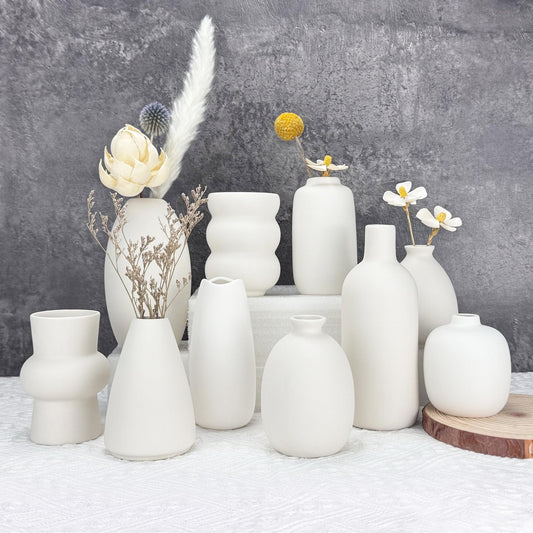 Collection of white ceramic vases with decorative elements on a textured surface and gray background