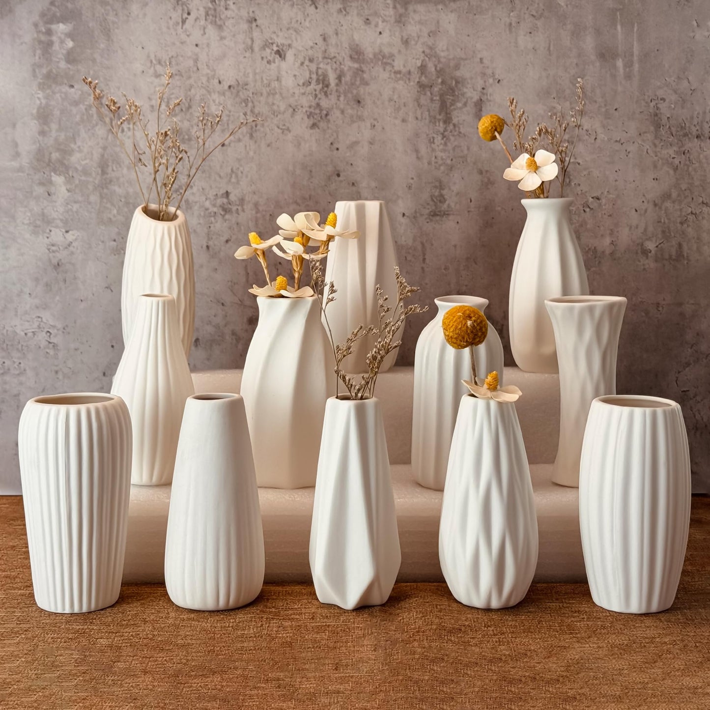 Collection of white ceramic vases with floral arrangements on a wooden surface.