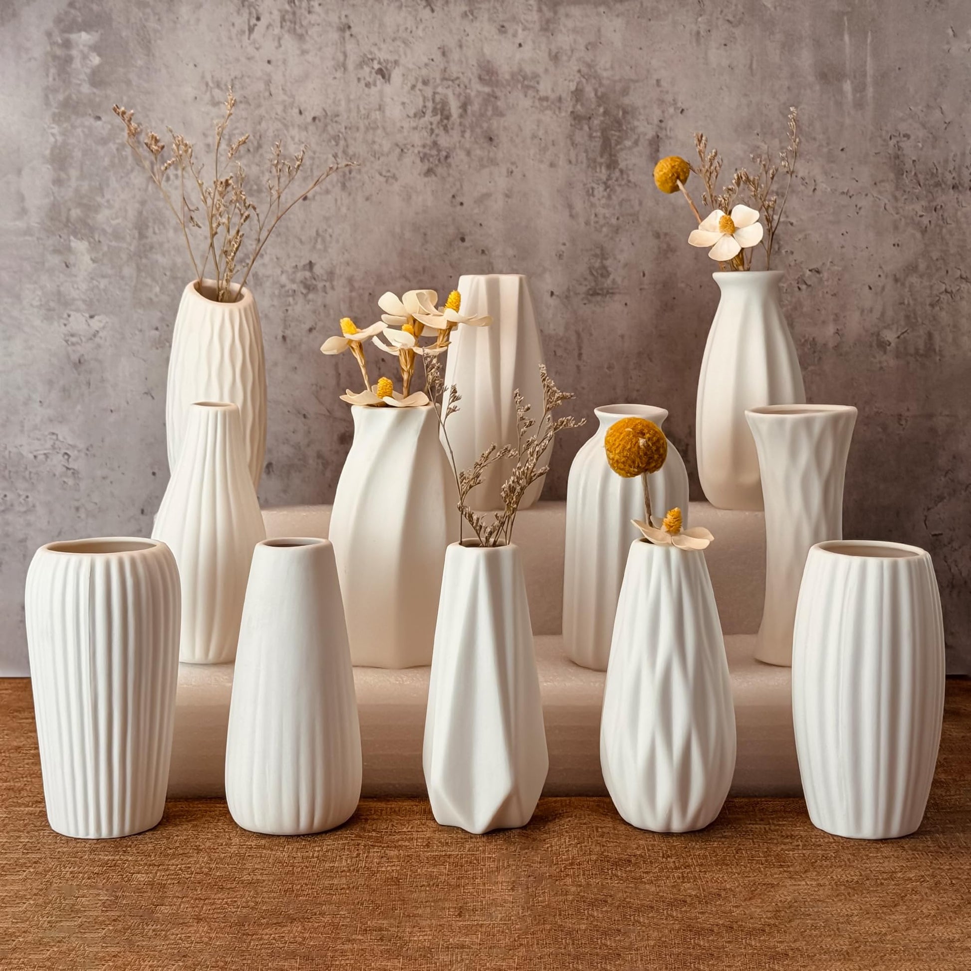 Collection of white ceramic vases with floral arrangements on a wooden surface.
