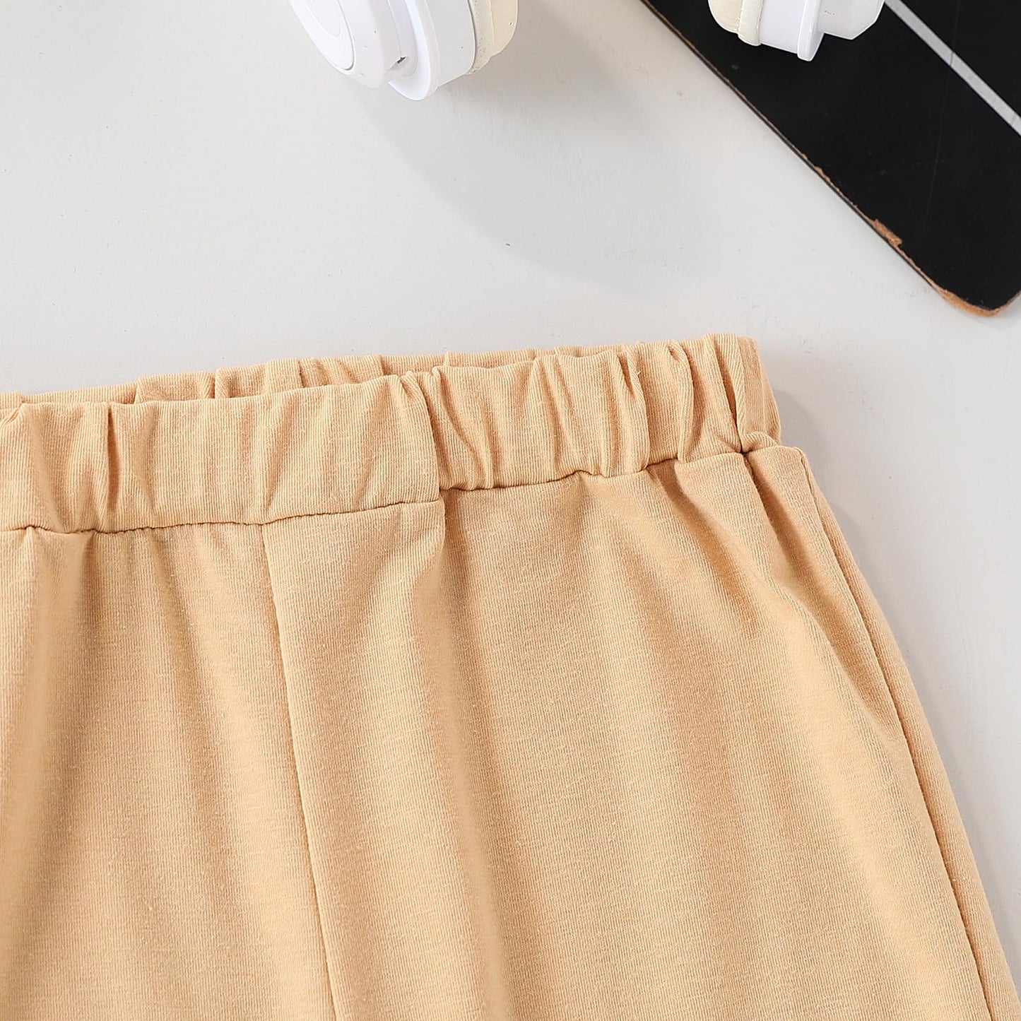 Beige pants on a white surface with a phone and headphones in the background