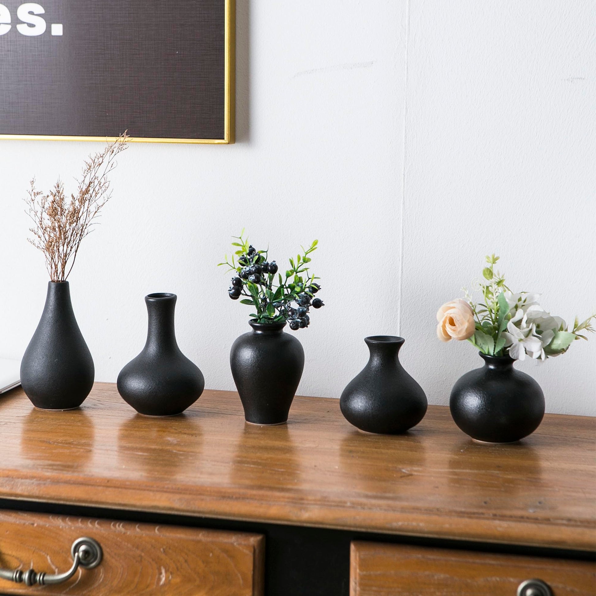 Five black vases with floral arrangements on a wooden surface.