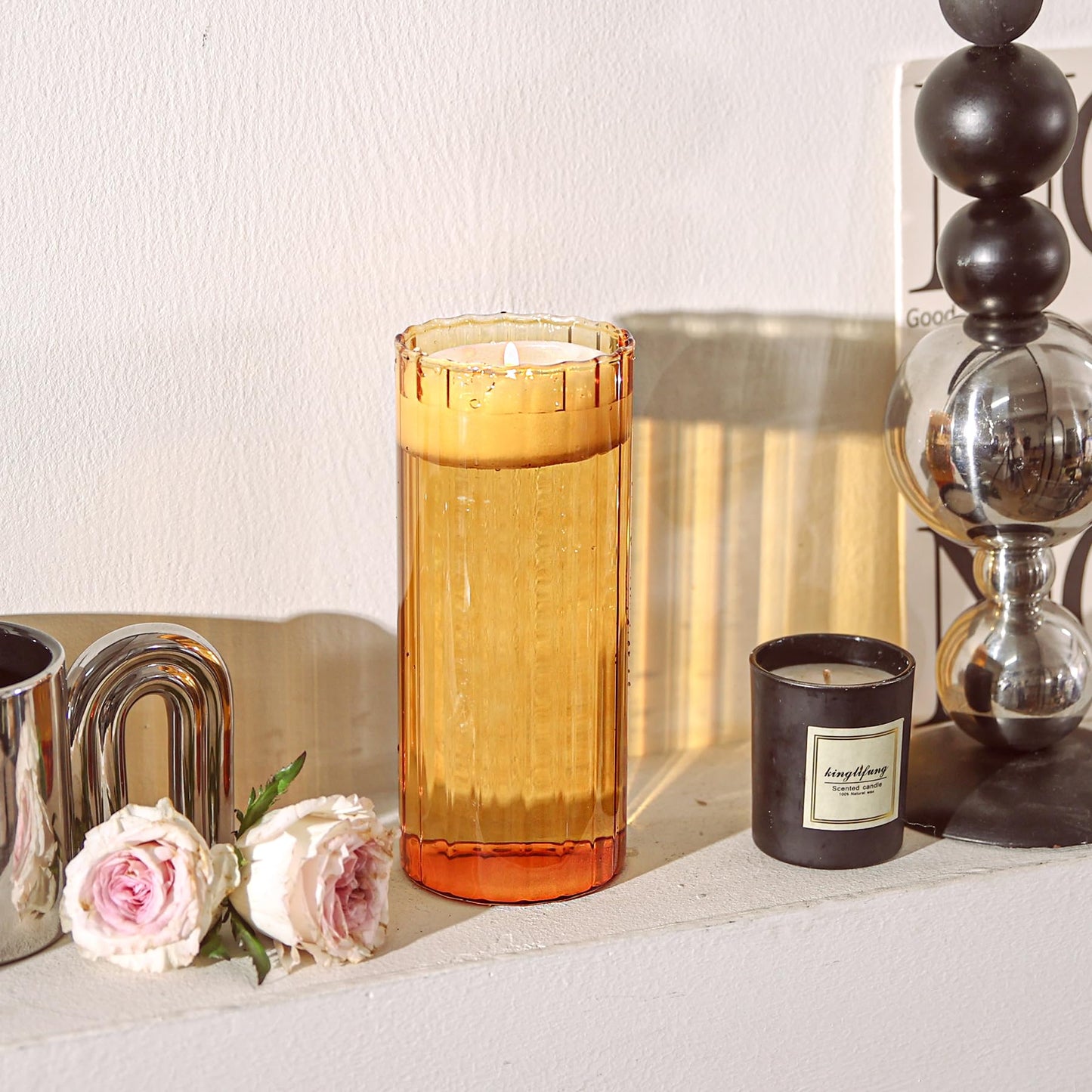 Candle in an orange glass holder on a surface with flowers and decorative items.