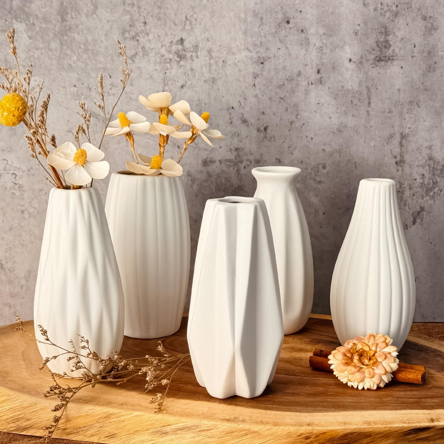 Set of white ceramic vases on a wooden surface with a concrete wall background