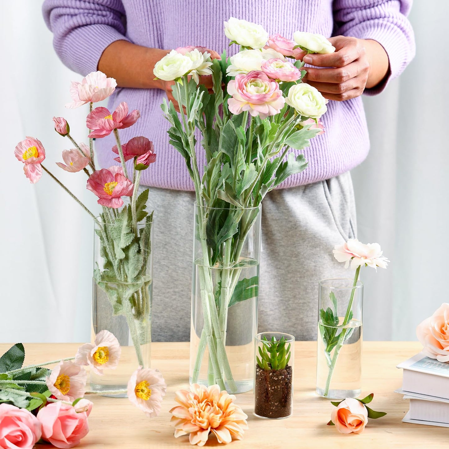 Person arranging flowers in vases on a table with a neutral background