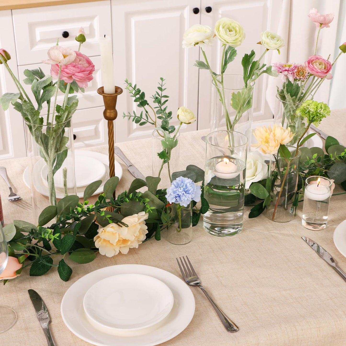 Elegant table setting with flowers, candles, and cutlery on a light-colored surface.