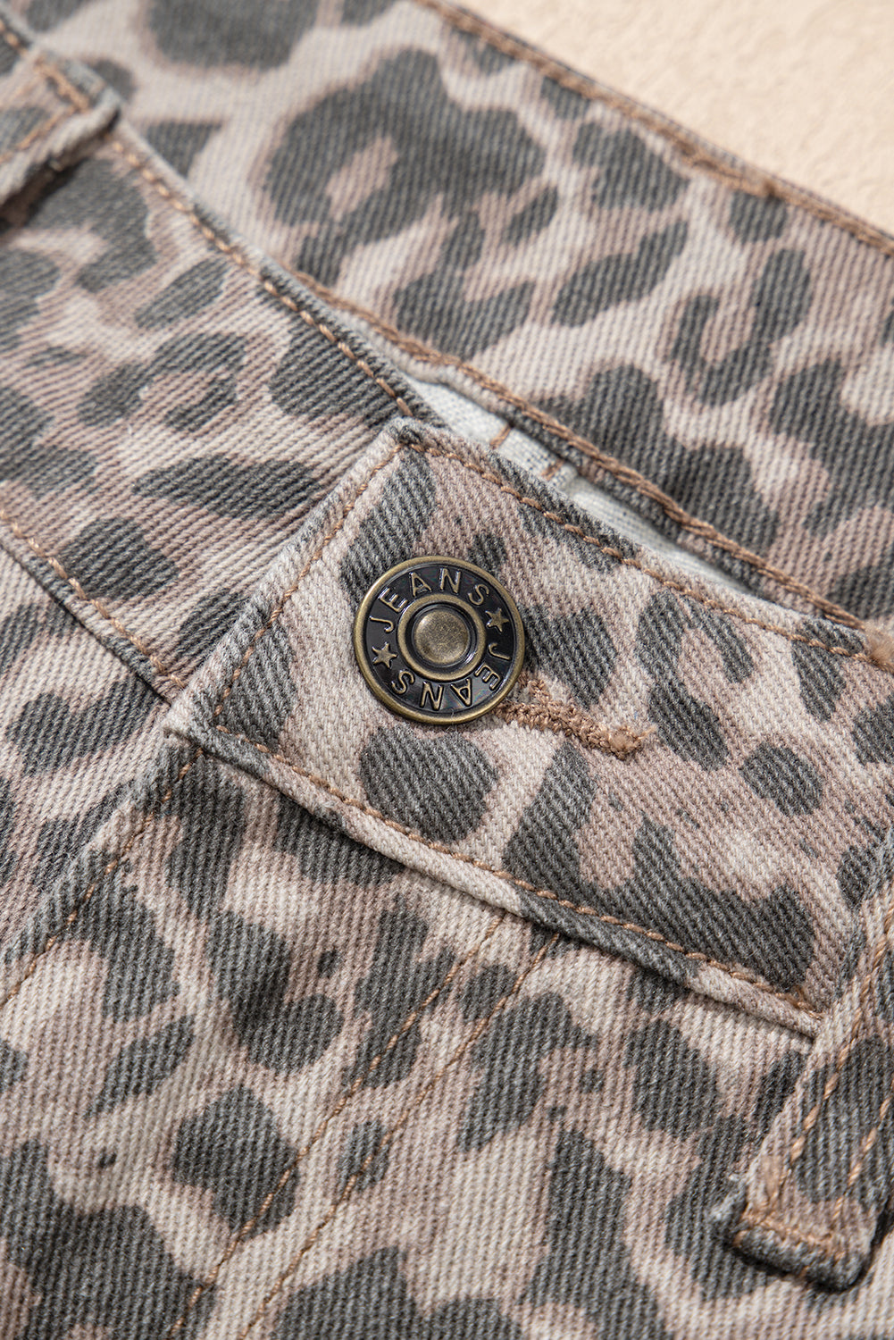 Close-up of a leopard print fabric with a button, featuring the brand 'R13' on a beige background.