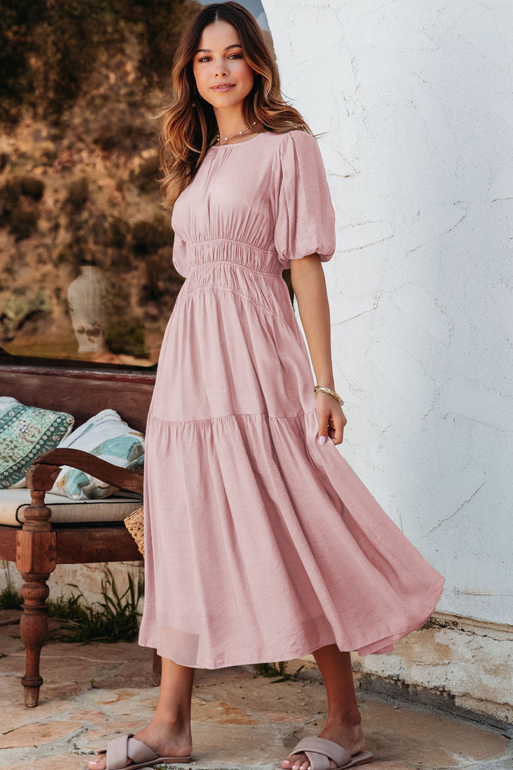 Woman wearing a pink dress standing in a rustic outdoor setting.