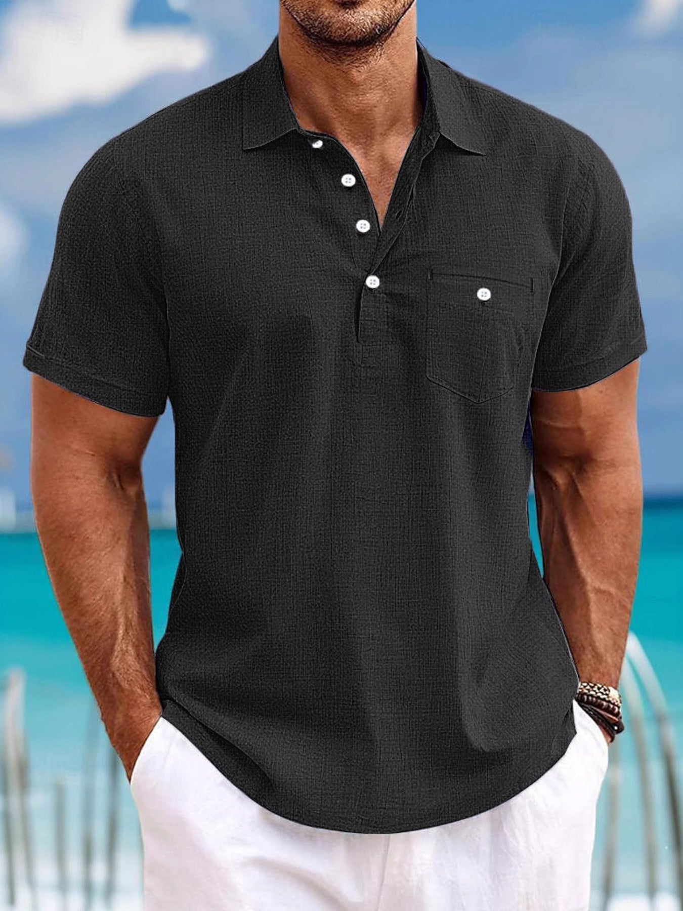 Man wearing a black textured polo shirt with a blurred beach background