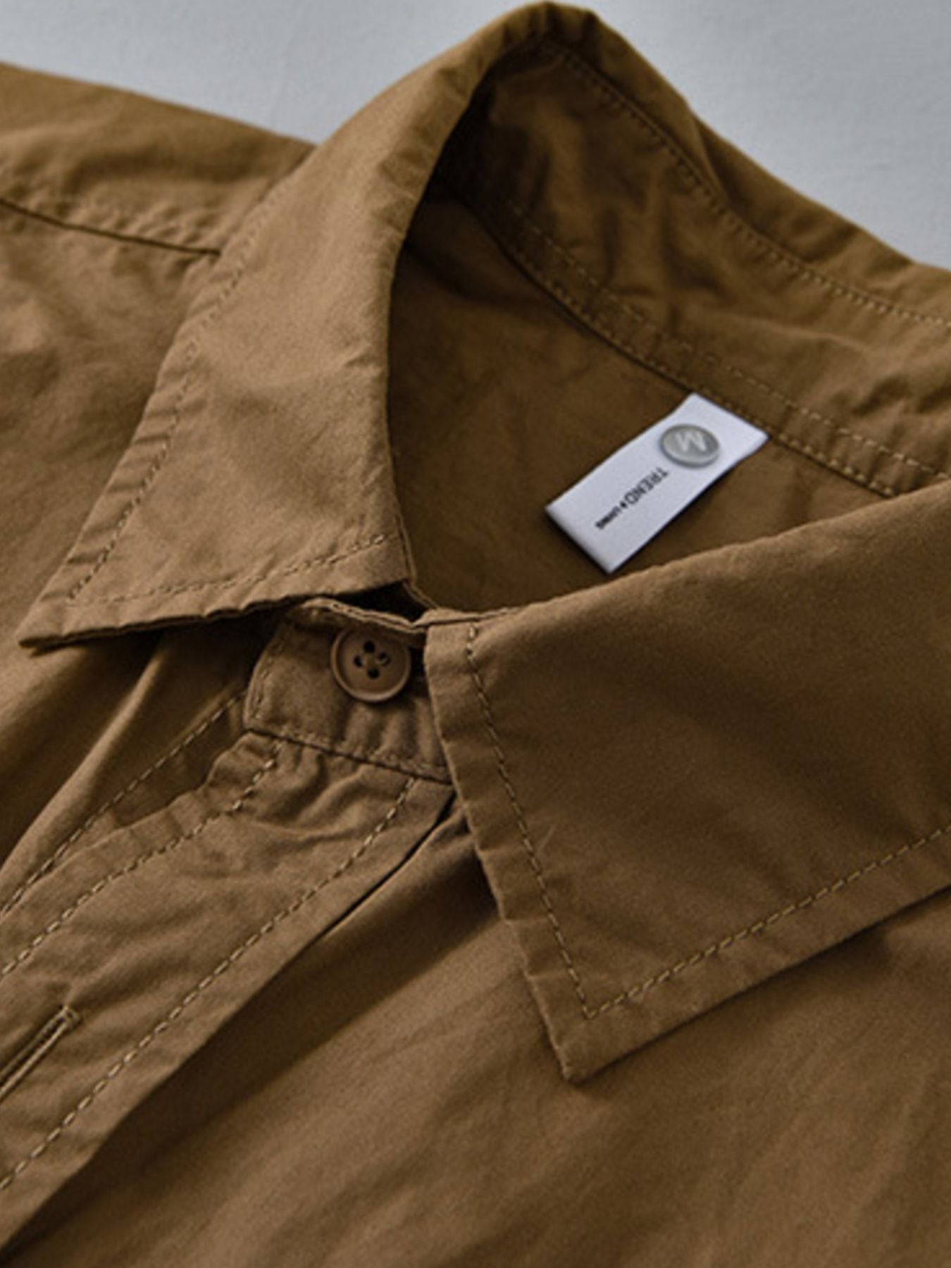 Close-up of a brown shirt collar with a visible brand label on a neutral background