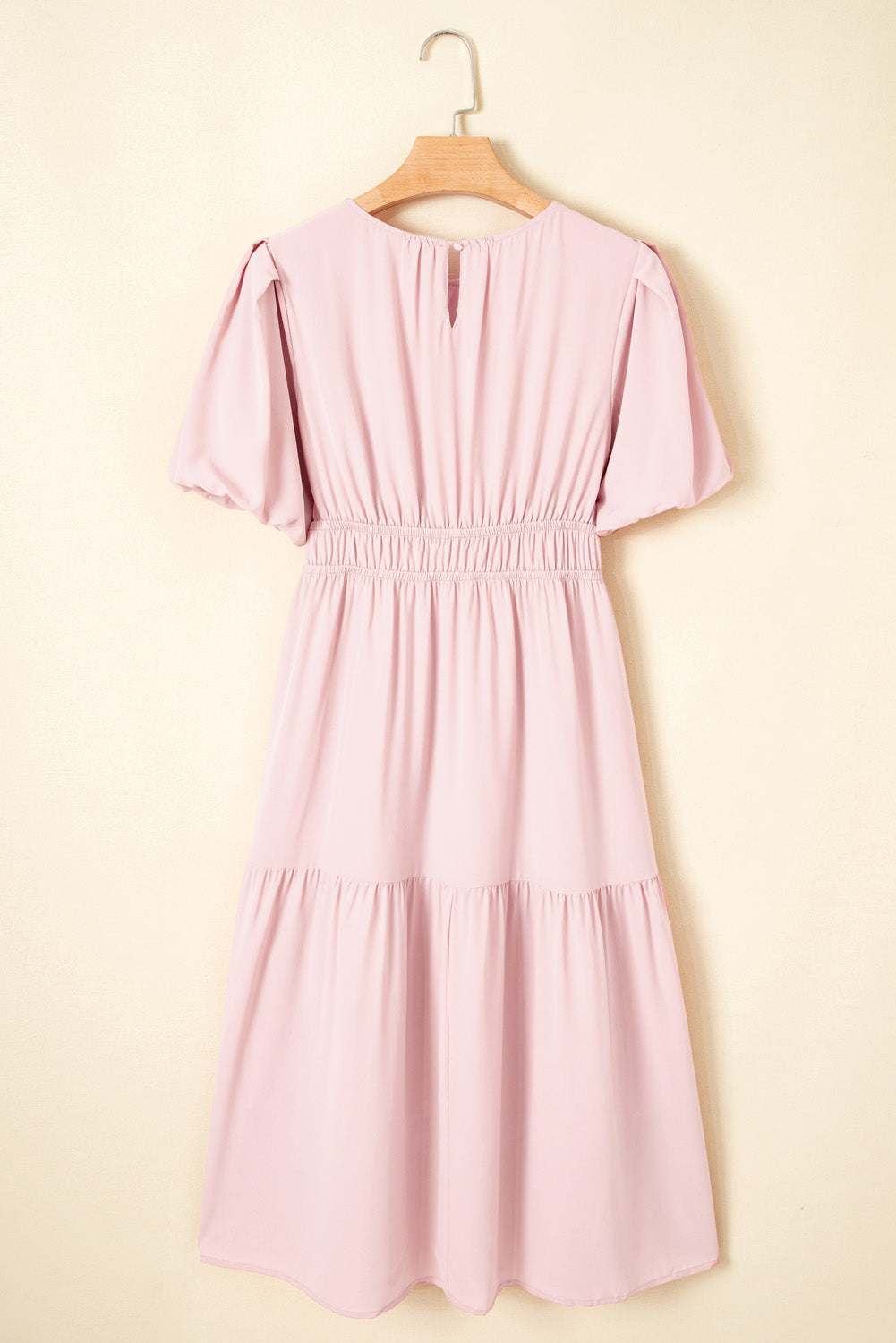 Pink dress on a wooden hanger against a beige background