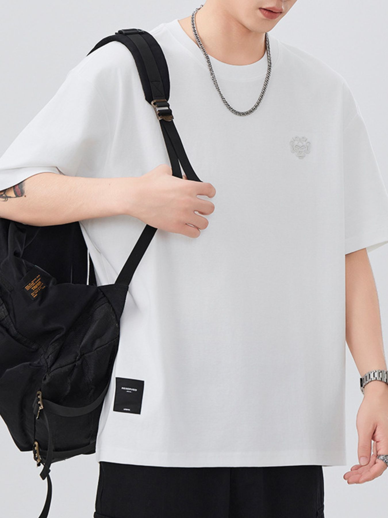 Person wearing a white oversized shirt with a black backpack on a light gray background