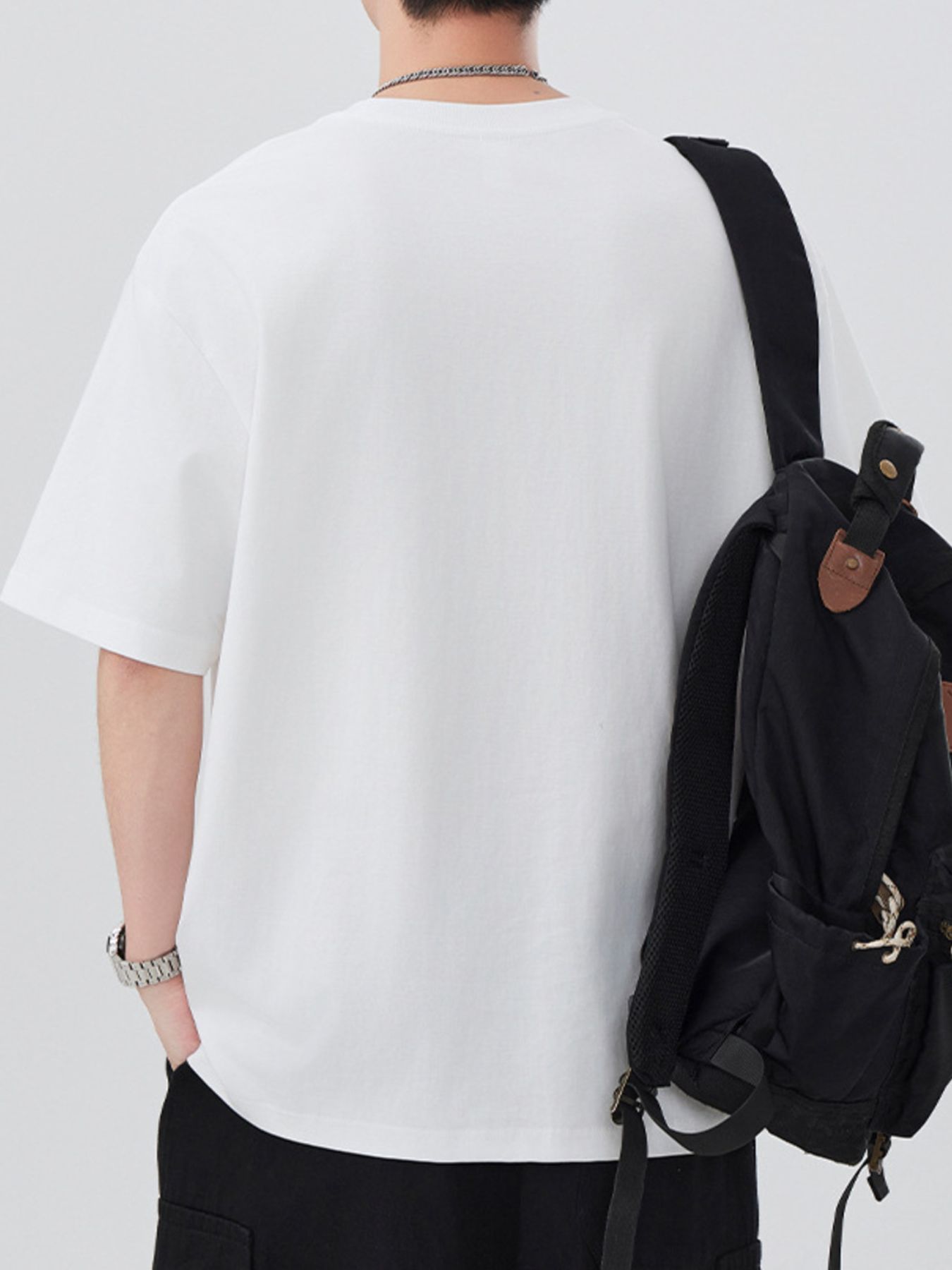 Person wearing a white t-shirt and black backpack on a plain background